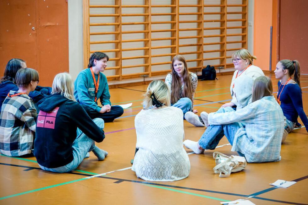 Nuoria istumassa salin lattialla ja keskustelemassa. Lattialla on kyniä ja lehtiöitä.